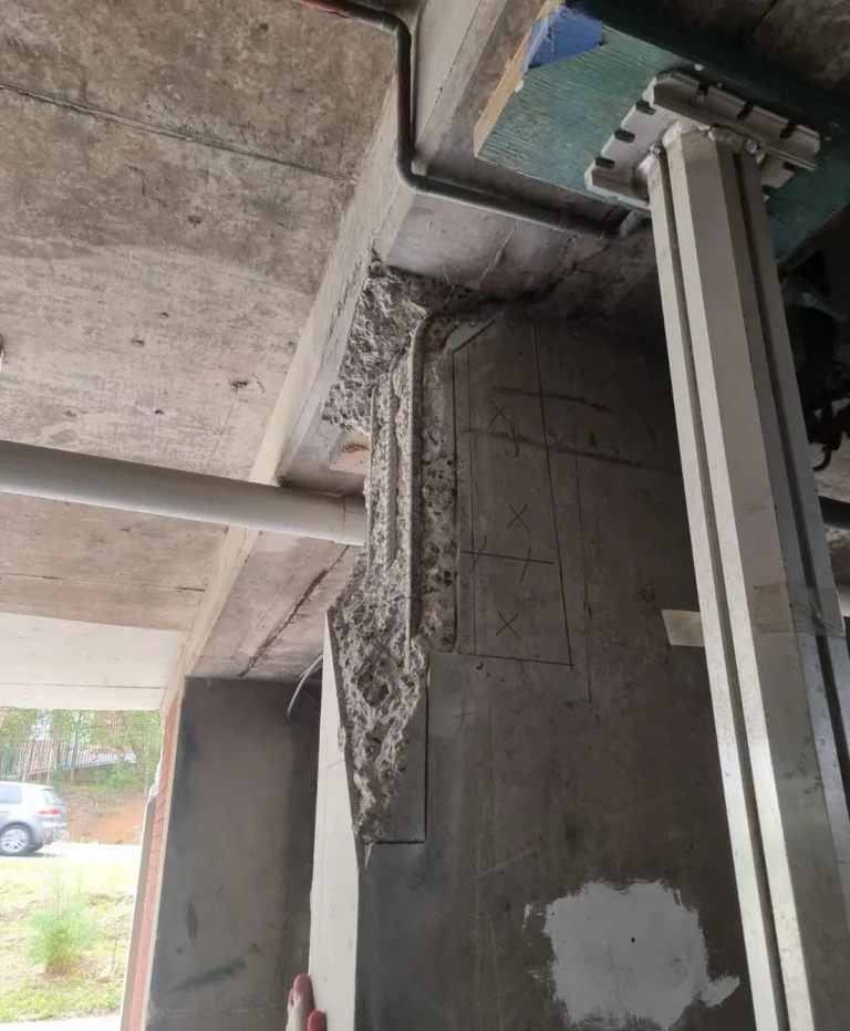Close-up of severe concrete spalling and exposed rebar at a slab-column interface caused by restrained thermal movement and lack of engineered joints.