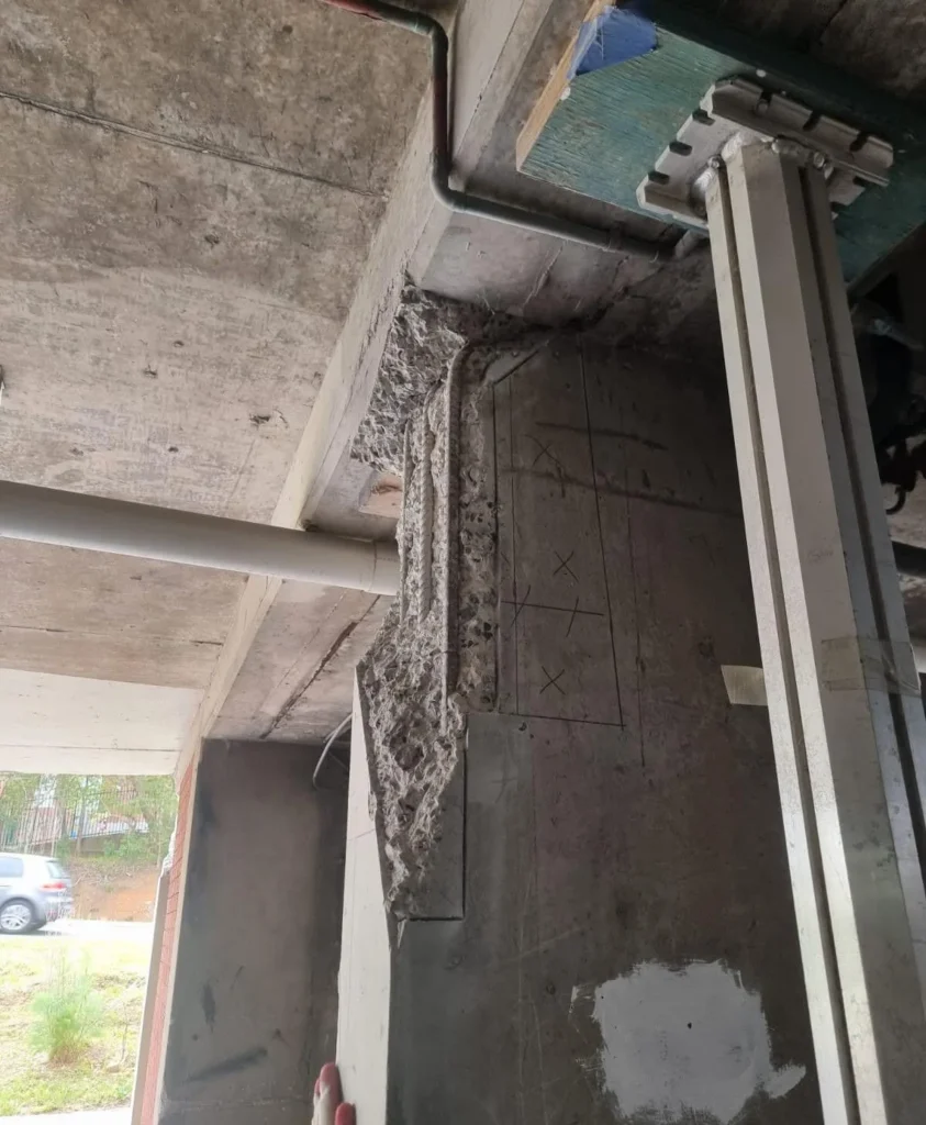 Close-up of severe concrete spalling and exposed rebar at a slab-column interface caused by restrained thermal movement and lack of engineered joints.